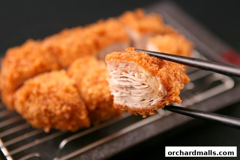 Close-up of crispy, layered pork cutlet being held by chopsticks.