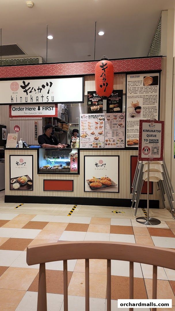 The Kimukatsu shop counter with a menu, food displays, and staff serving customers.