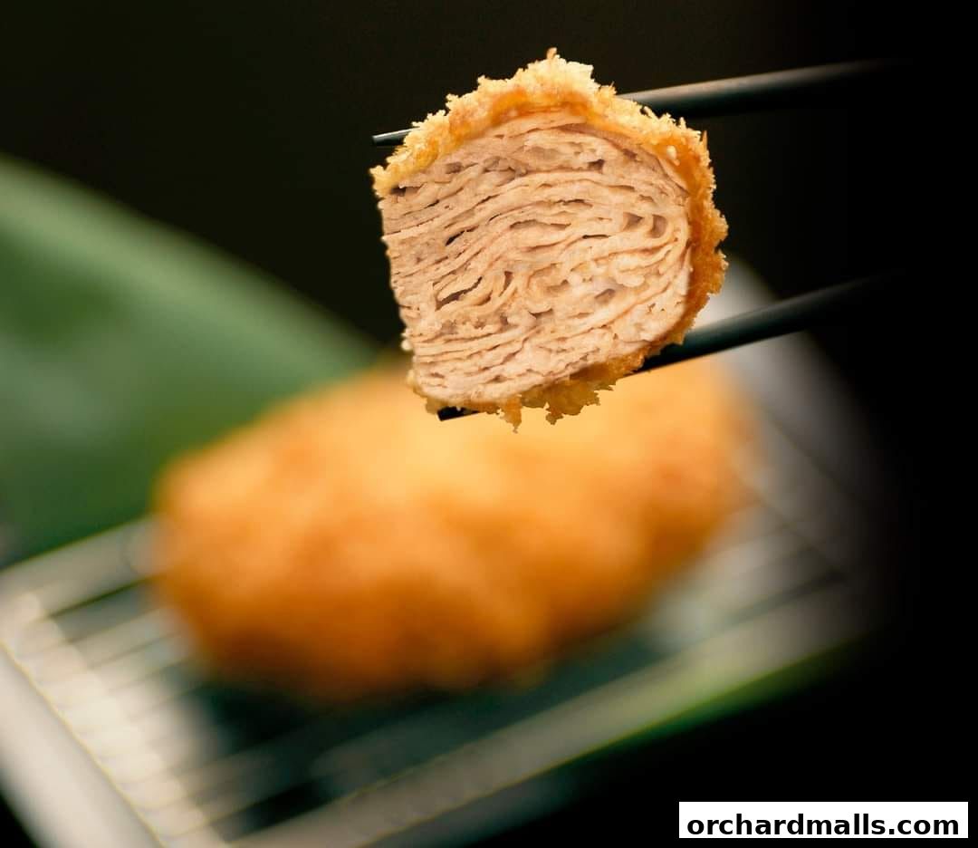 A close-up shot of a layered, deep-fried cutlet held by chopsticks.