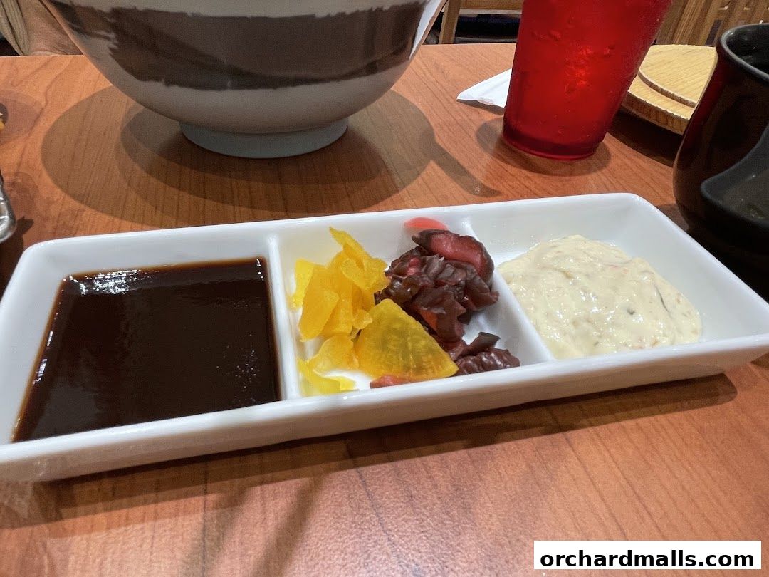 A white dish with three compartments containing sauce, pickles, and a creamy dip.