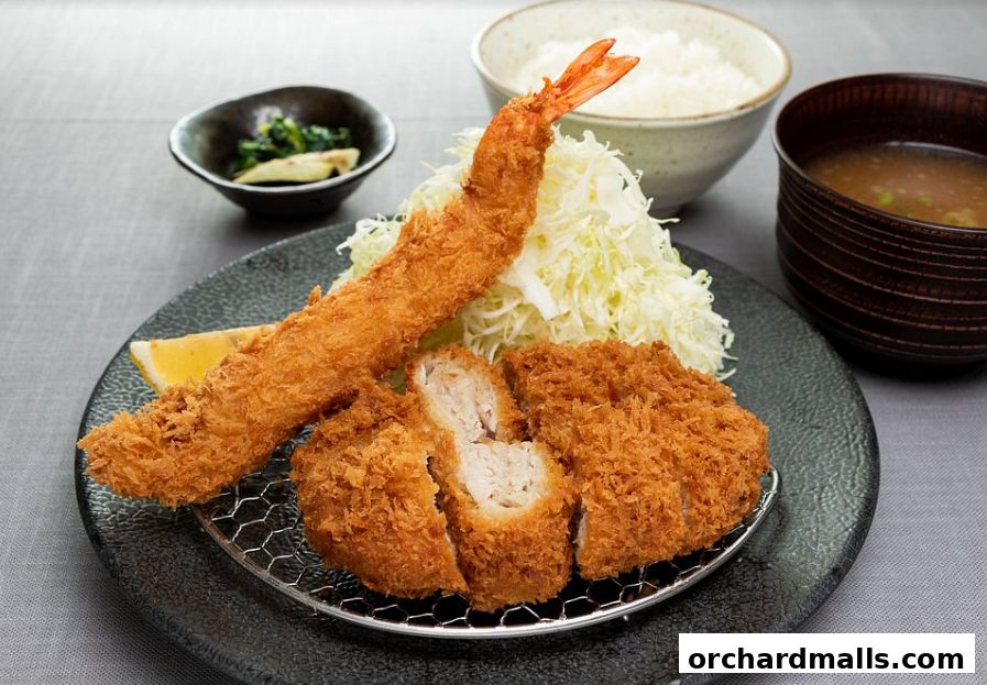 A delicious meal featuring crispy fried pork cutlet, a large shrimp, rice, and miso soup.