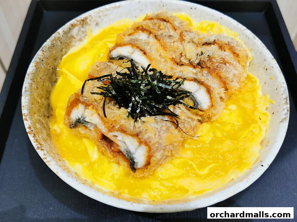 A close-up of a delicious dish featuring crispy fried eel over scrambled eggs and rice.