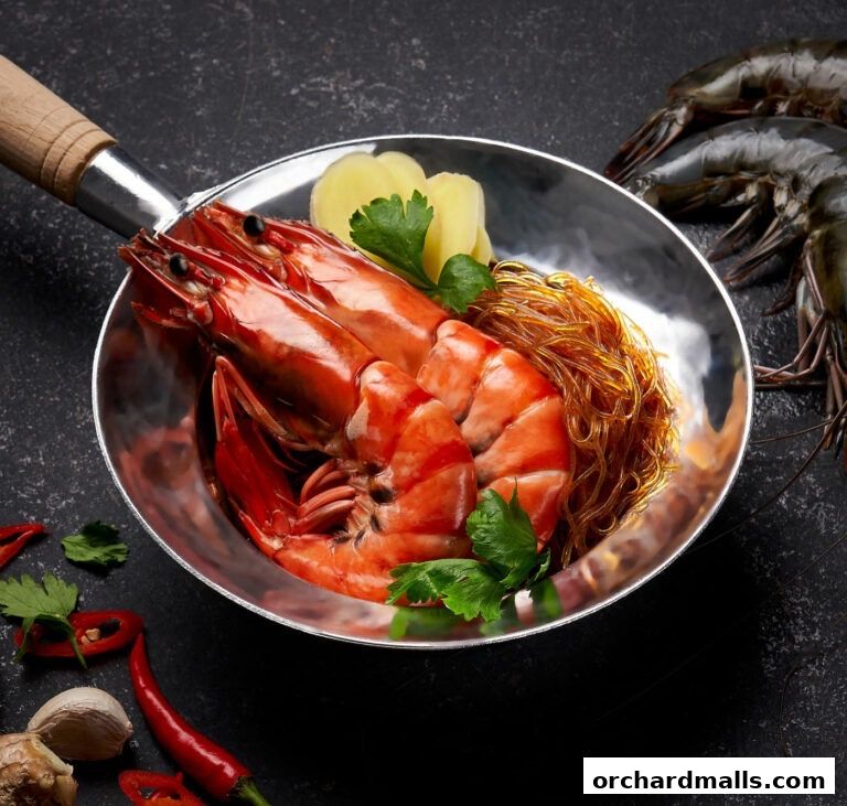 A close-up of a pan with cooked prawns and glass noodles, garnished with ginger and parsley.
