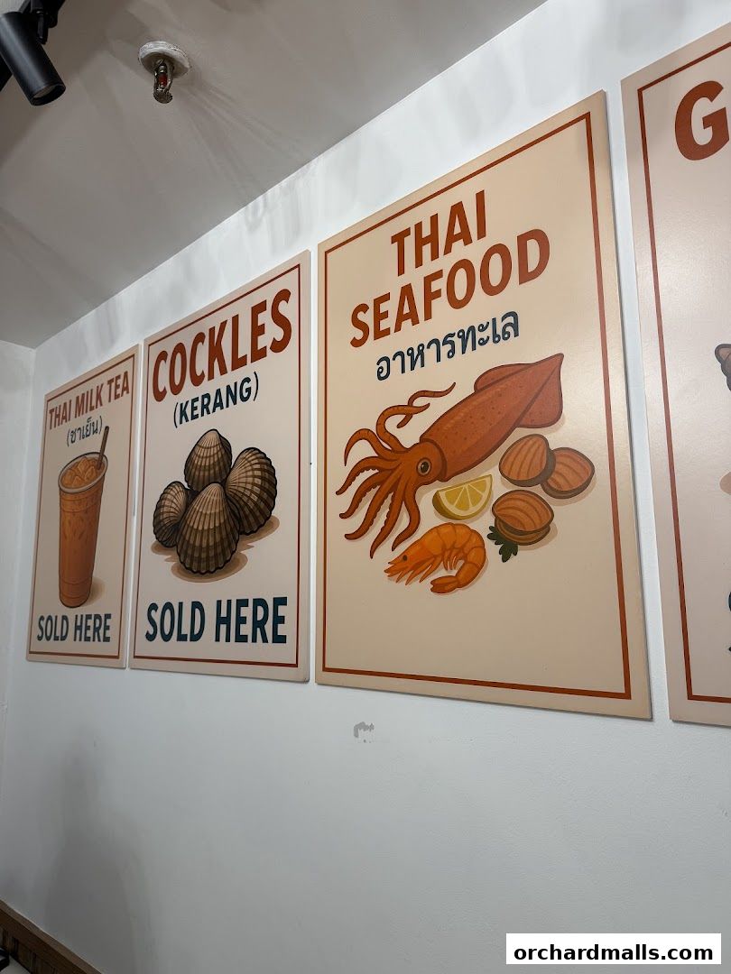 Signs for Thai Milk Tea, Cockles, and Thai Seafood are displayed on a white wall.