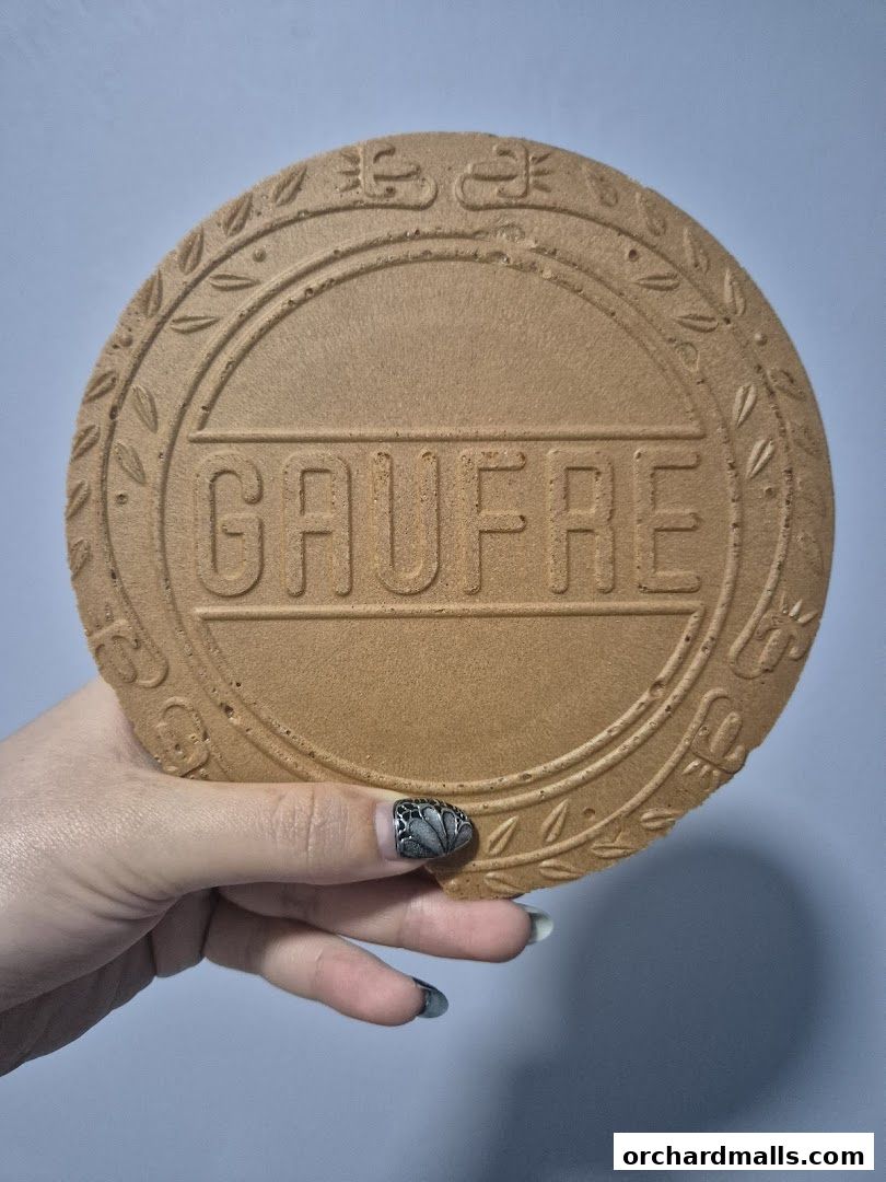 A hand holds a round, embossed waffle cookie with the word GAUFRE in the center.