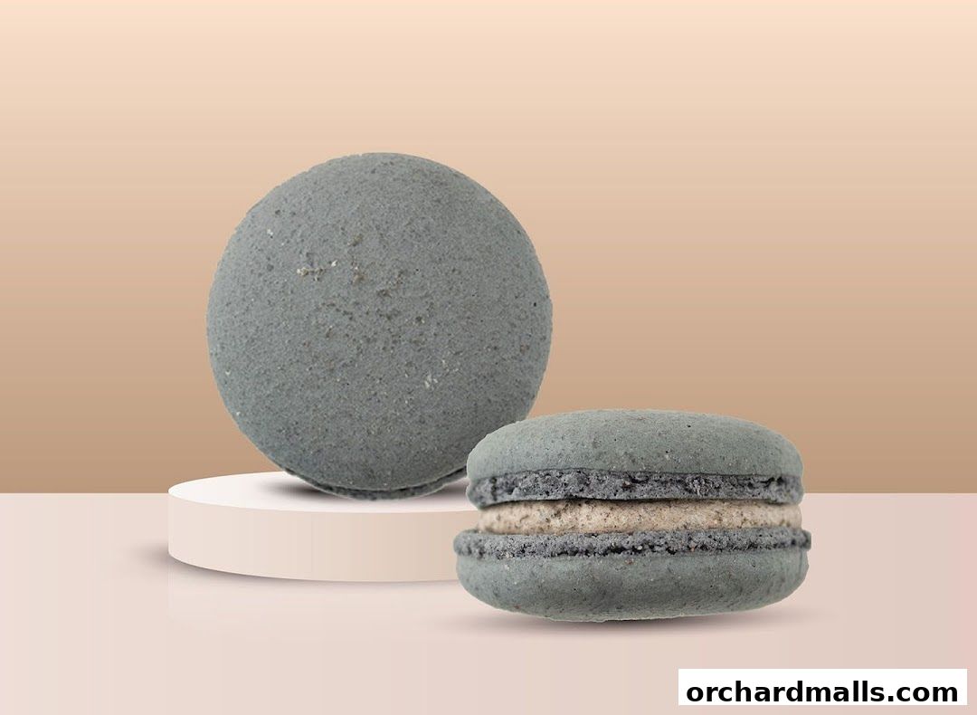 Two grey macarons, one whole and one filled, displayed on a pedestal.