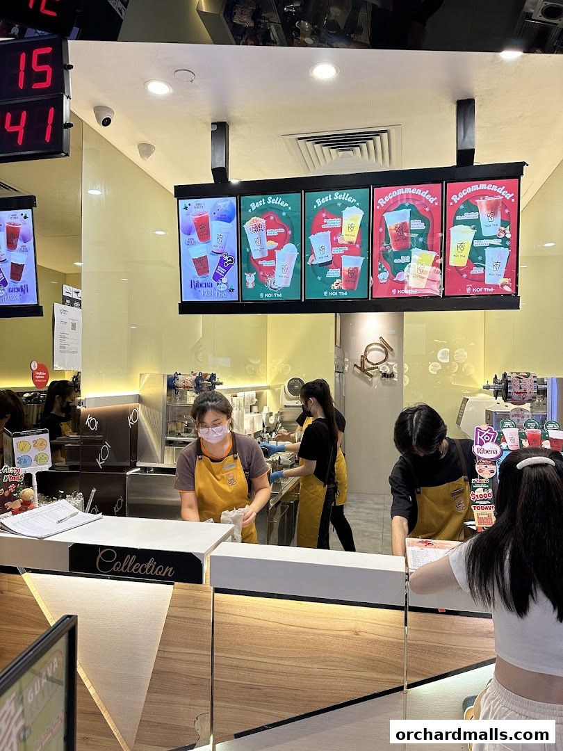 Staff members serving customers at the KOI Thé counter with digital displays showing drink promotions.