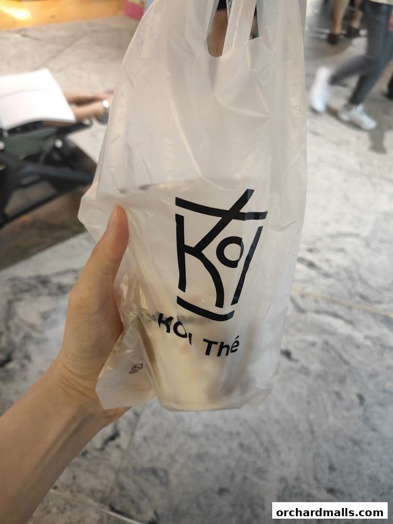 A hand holds a transparent plastic bag with the KOI Thé logo and a drink inside.