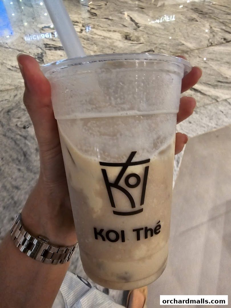 A hand holds a KOI Thé bubble tea cup with the brand logo visible.
