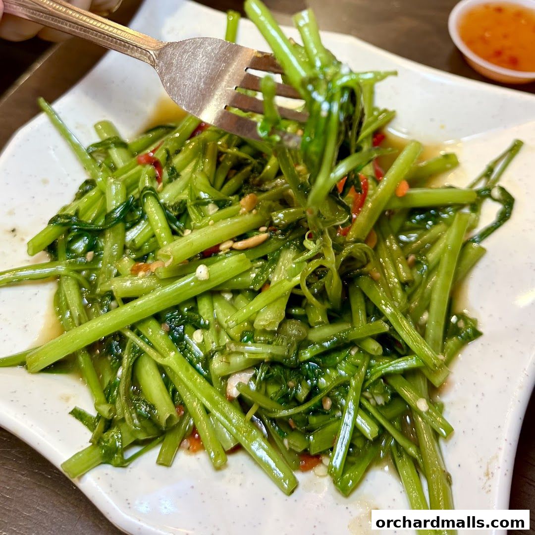 A fork lifts a portion of stir-fried water spinach with chili and garlic.