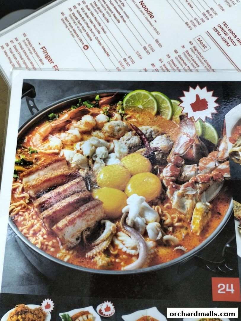 A close-up of a Thai noodle soup dish with various meats and seafood, alongside a menu.