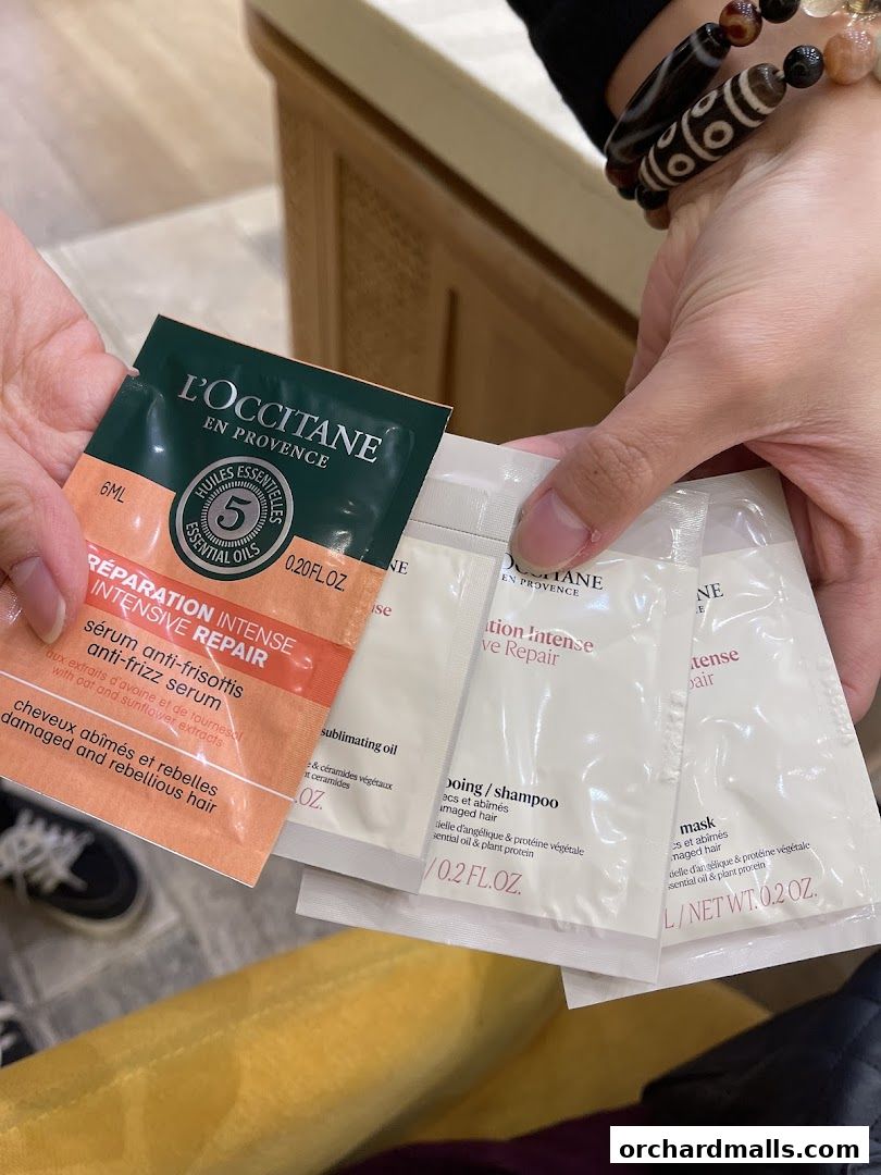 Hands holding L'Occitane Intensive Repair hair care sample sachets.