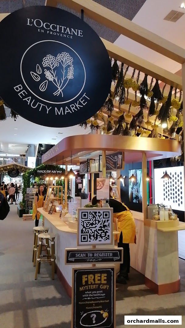 L'Occitane Beauty Market stall with staff, products, and promotional signage.