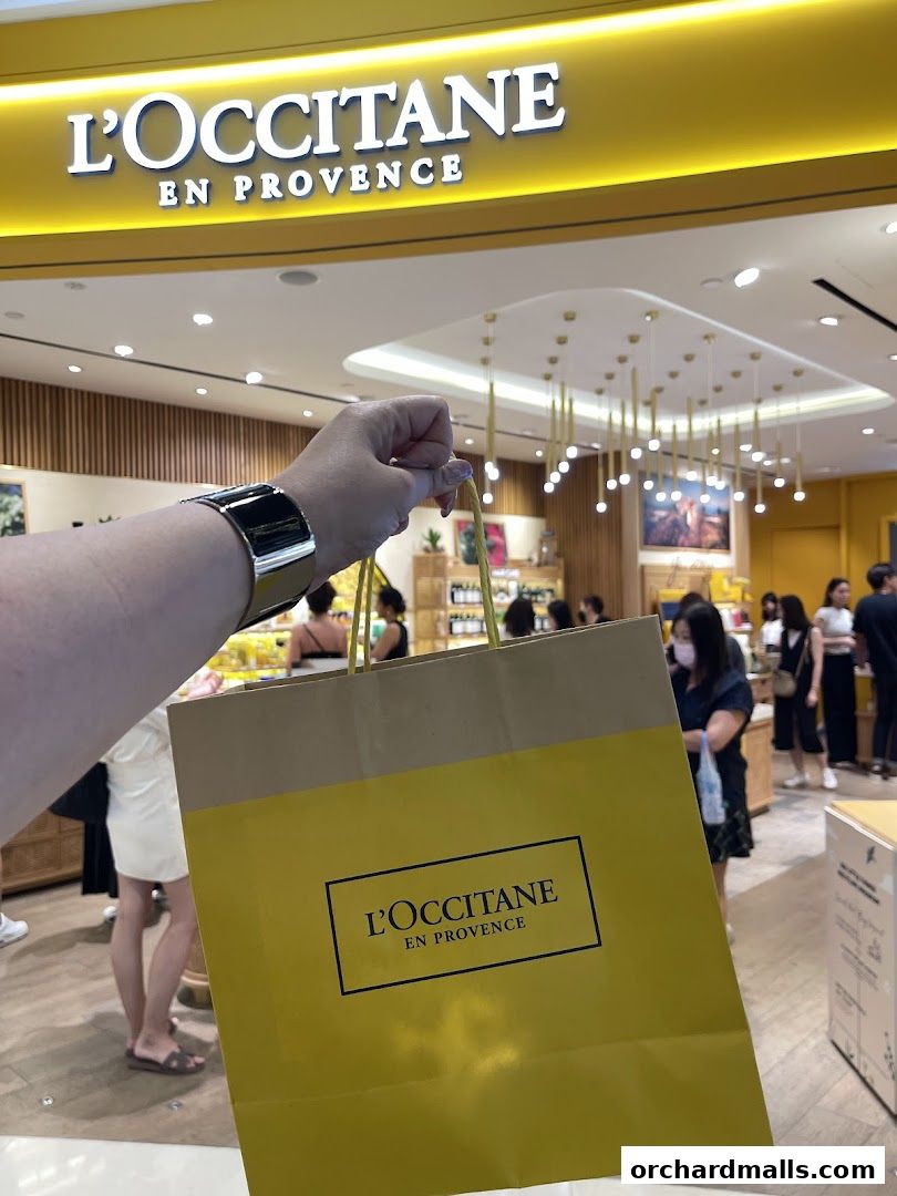 A person holds a L'Occitane shopping bag in front of the store.