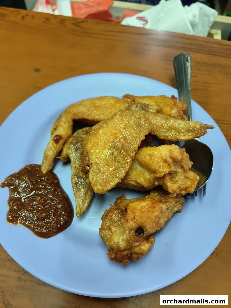 A plate of crispy fried chicken wings with a side of chili sauce.