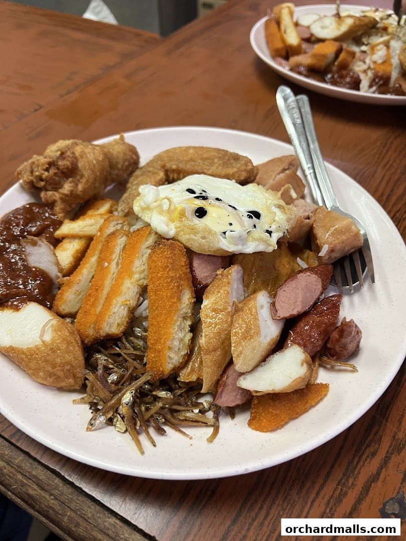 A plate of nasi lemak with fried chicken, egg, sausages, and anchovies.