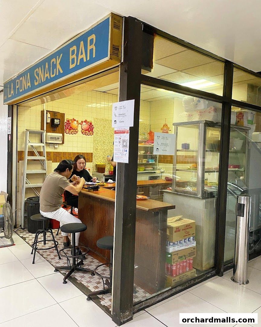 La Pona Snack Bar Nasi Lemak features a counter with customers and a display of drinks.