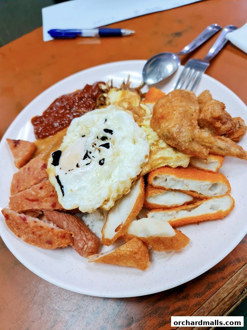 A plate of Nasi Lemak with fried chicken wing, fried egg, and various fried sides.