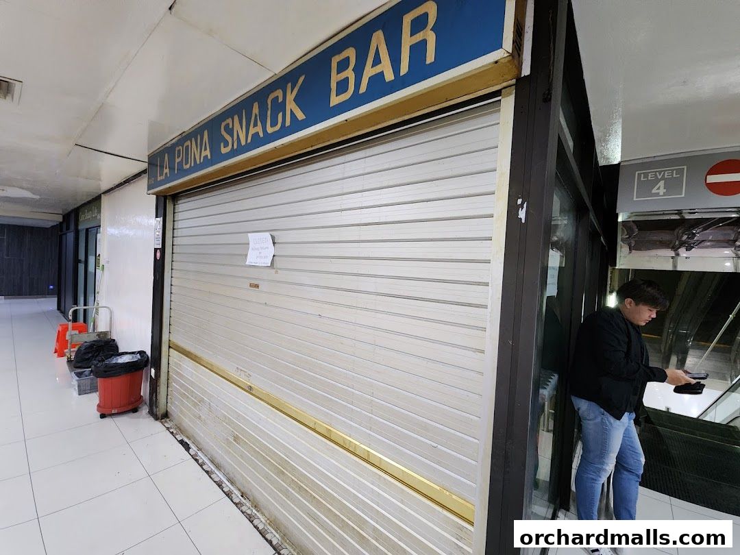 La Pona Snack Bar Nasi Lemak shop front with a closed roller shutter and a person standing nearby.