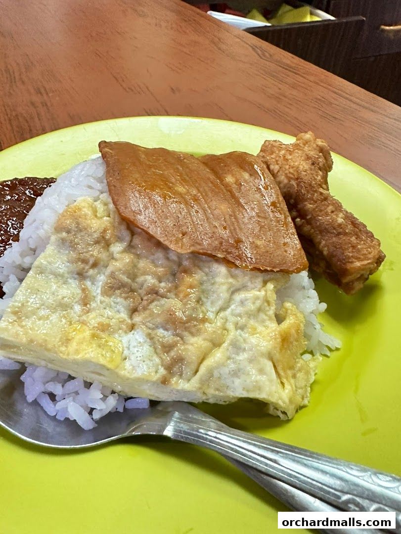 A plate of Nasi Lemak with rice, fried egg, fried chicken, and sambal.