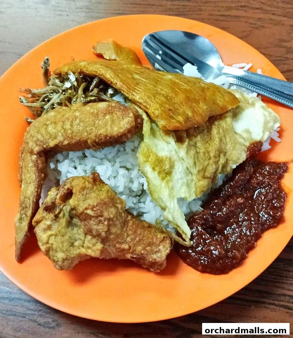 A plate of Nasi Lemak with fried chicken, egg, anchovies, and sambal.
