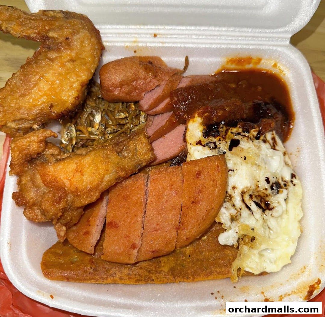 A takeaway container filled with Nasi Lemak, featuring fried chicken, sausage, egg, and anchovies.