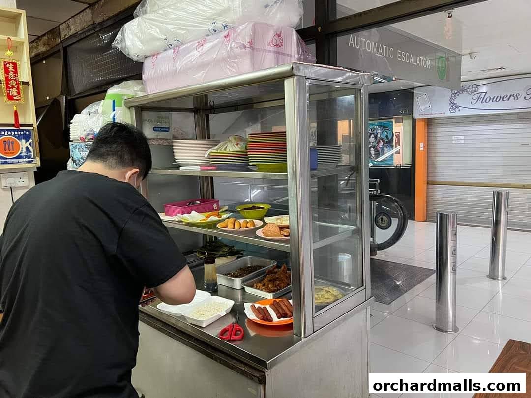 A person preparing food at a stall with various dishes displayed.