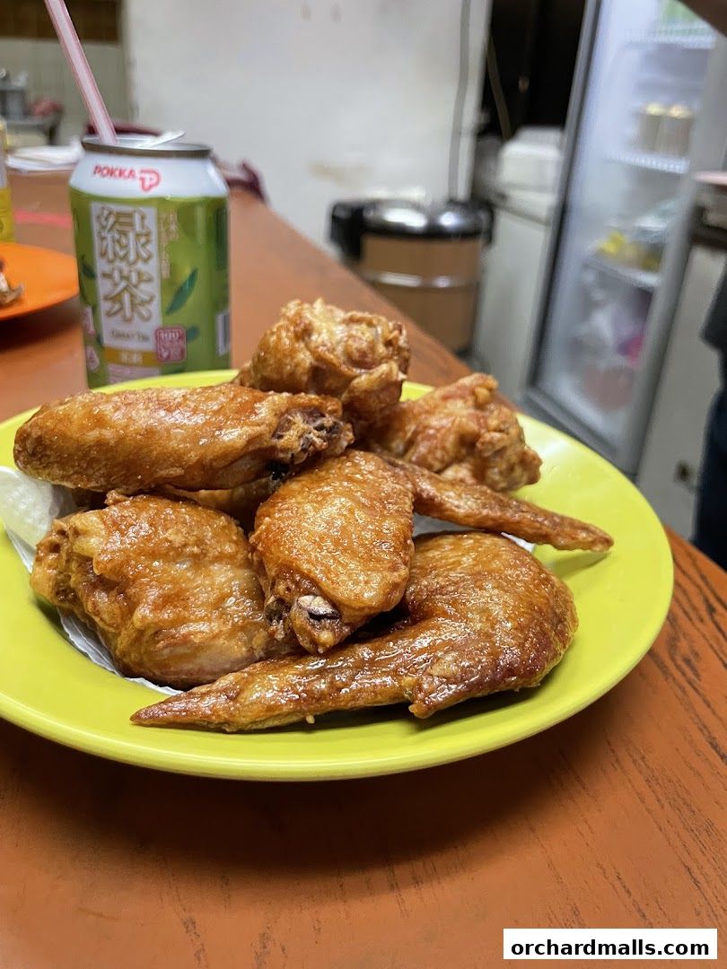 A plate of golden-brown fried chicken wings served with a can of green tea.