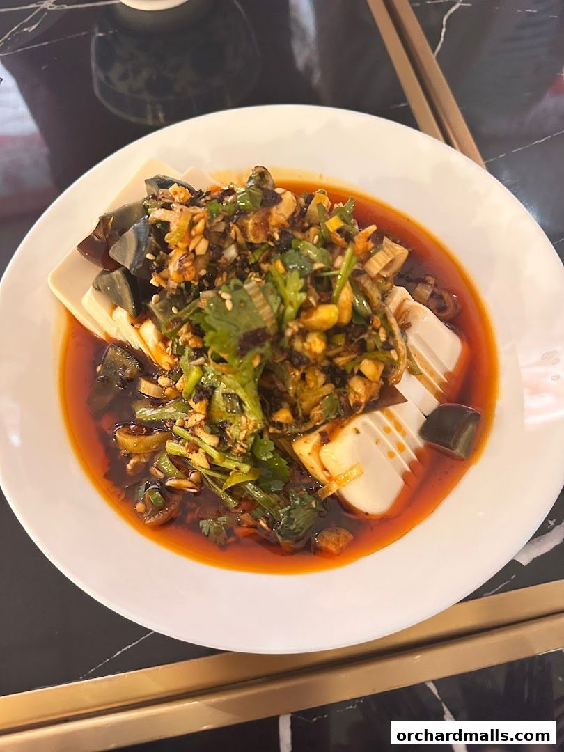 A plate of chilled tofu with preserved eggs and chili oil, garnished with herbs.