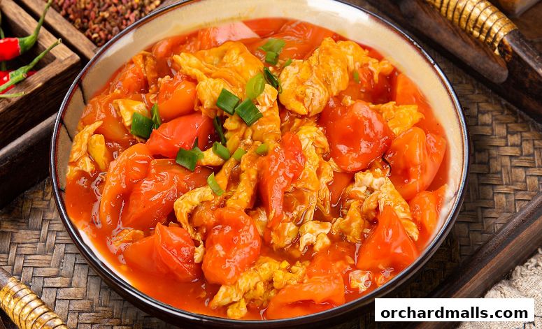 A close-up shot of a delicious tomato and egg stir-fry dish, garnished with green onions.