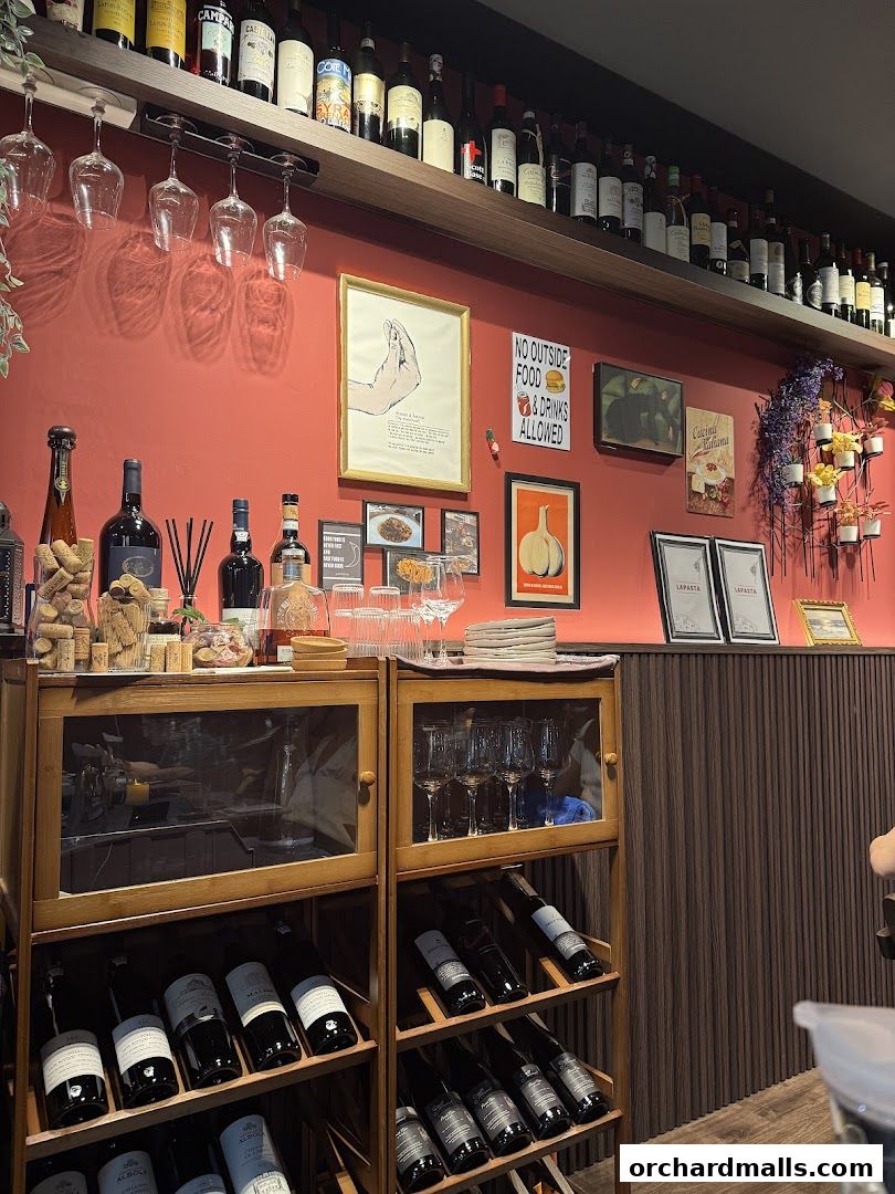 Interior shot of LaPasta restaurant with wine bottles, glasses, and decor on a red wall.