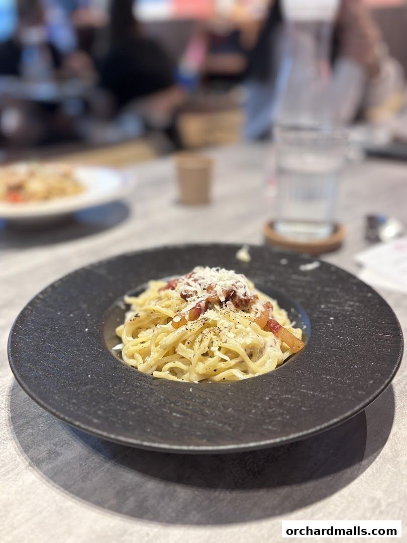 A close-up of a delicious spaghetti carbonara dish served in a dark bowl.