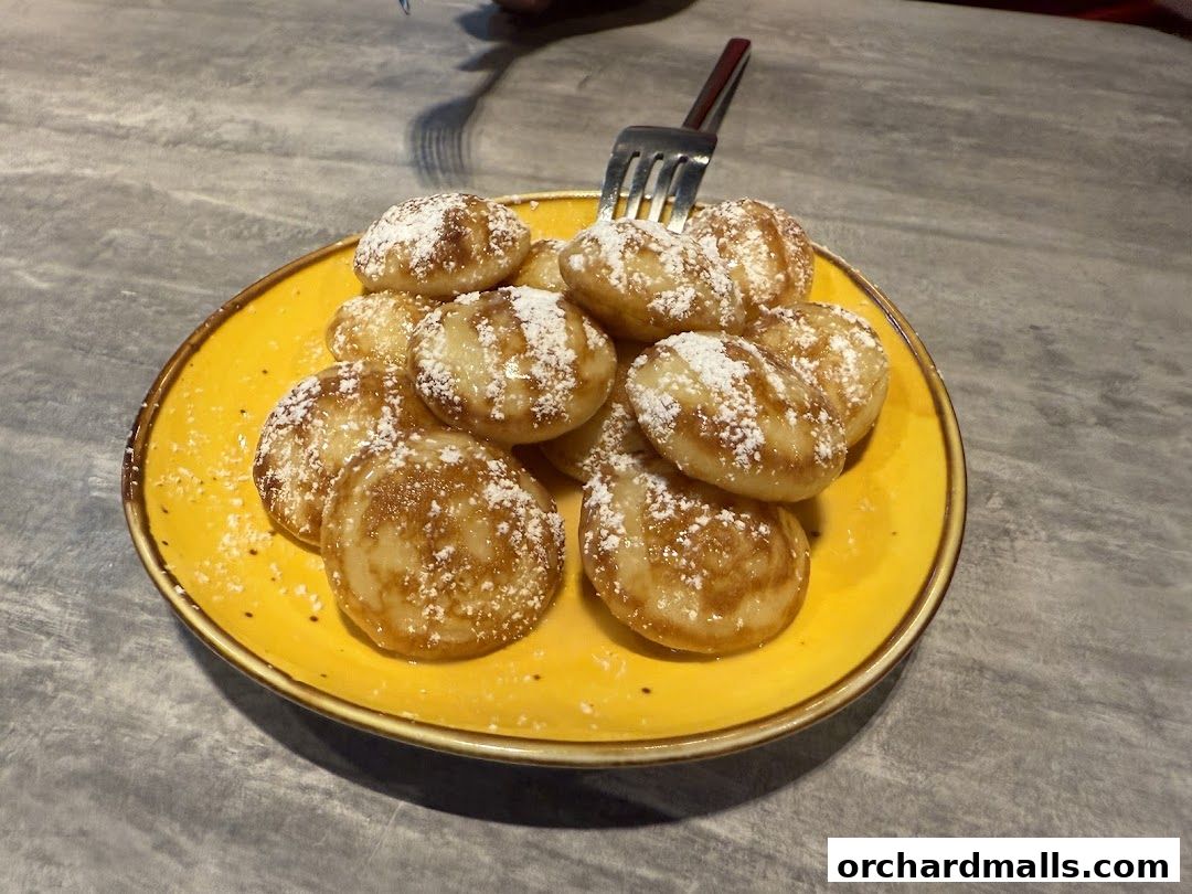 A plate of mini pancakes dusted with powdered sugar and drizzled with syrup.
