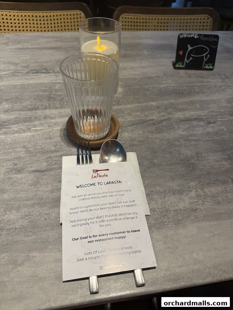 A table setting at LaPasta restaurant with a welcome card, cutlery, and a candle.