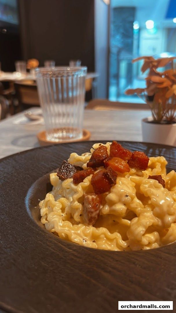 A close-up of a creamy pasta dish with crispy toppings in a dark bowl.