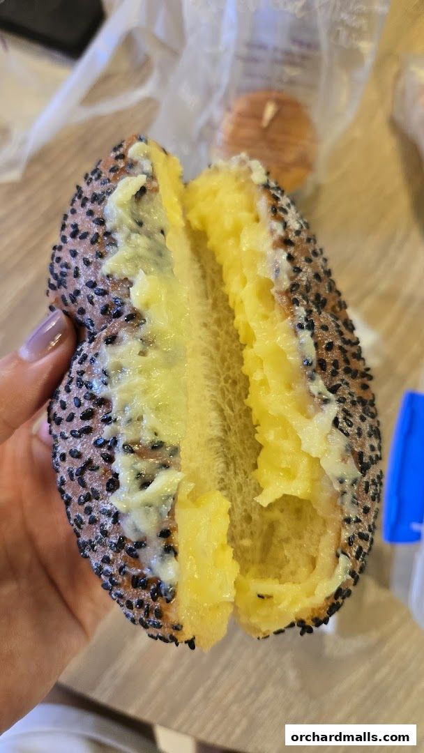 A close-up of a pastry filled with creamy yellow filling, topped with black sesame seeds.