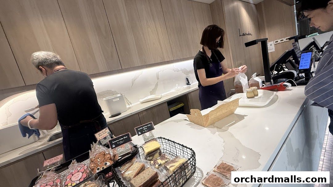 Staff serving customers at the counter of a bakery with various pastries on display.