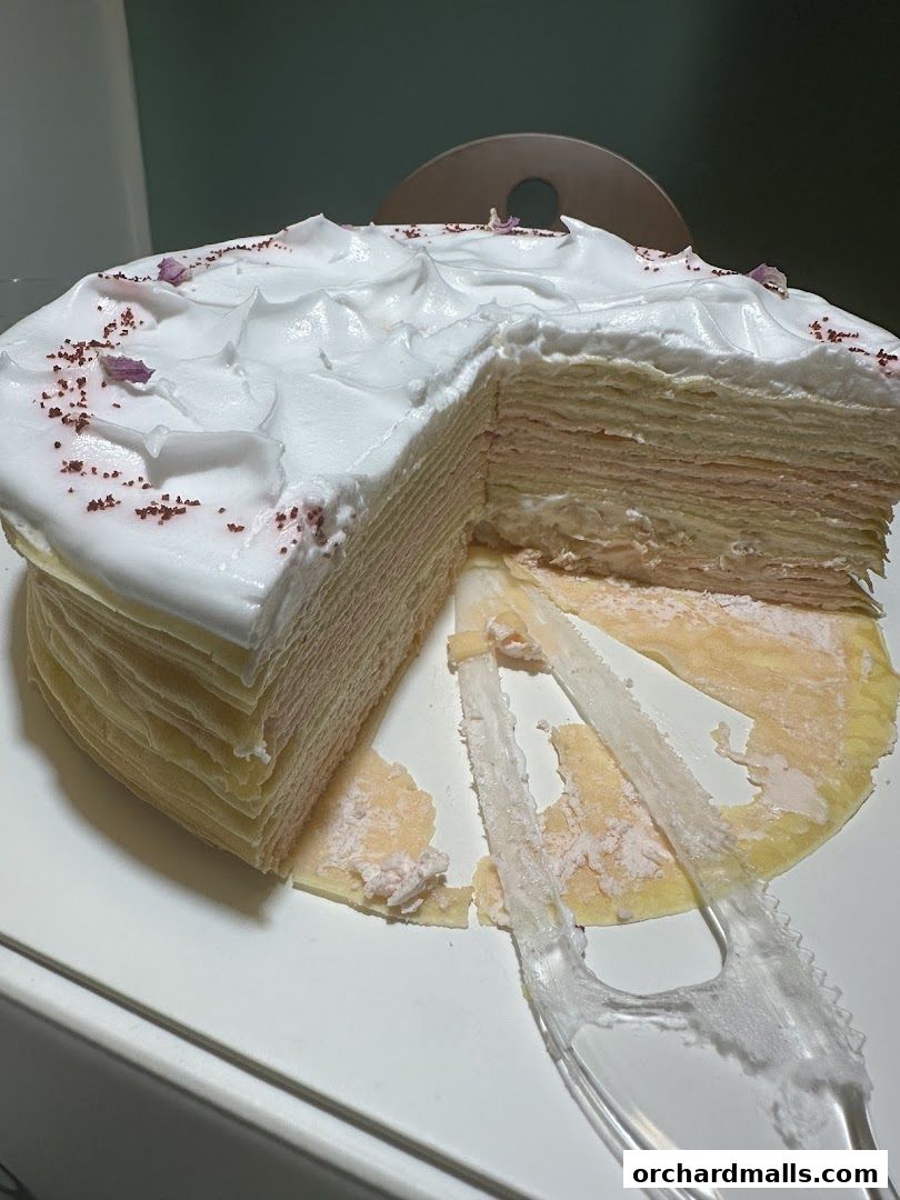 A slice of a layered crepe cake with white frosting and pink filling, garnished with sprinkles and petals.