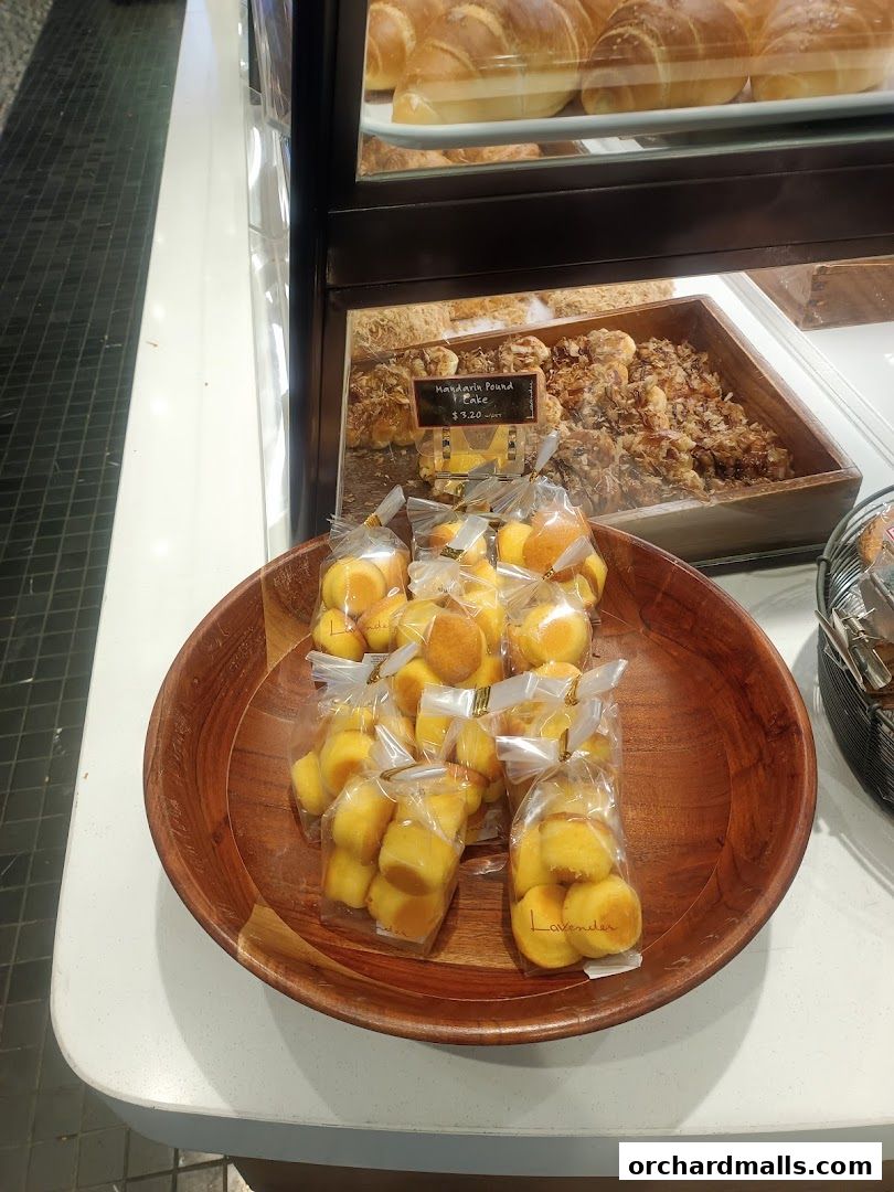 A wooden bowl filled with individually packaged mini cakes and a display of pastries in the background.