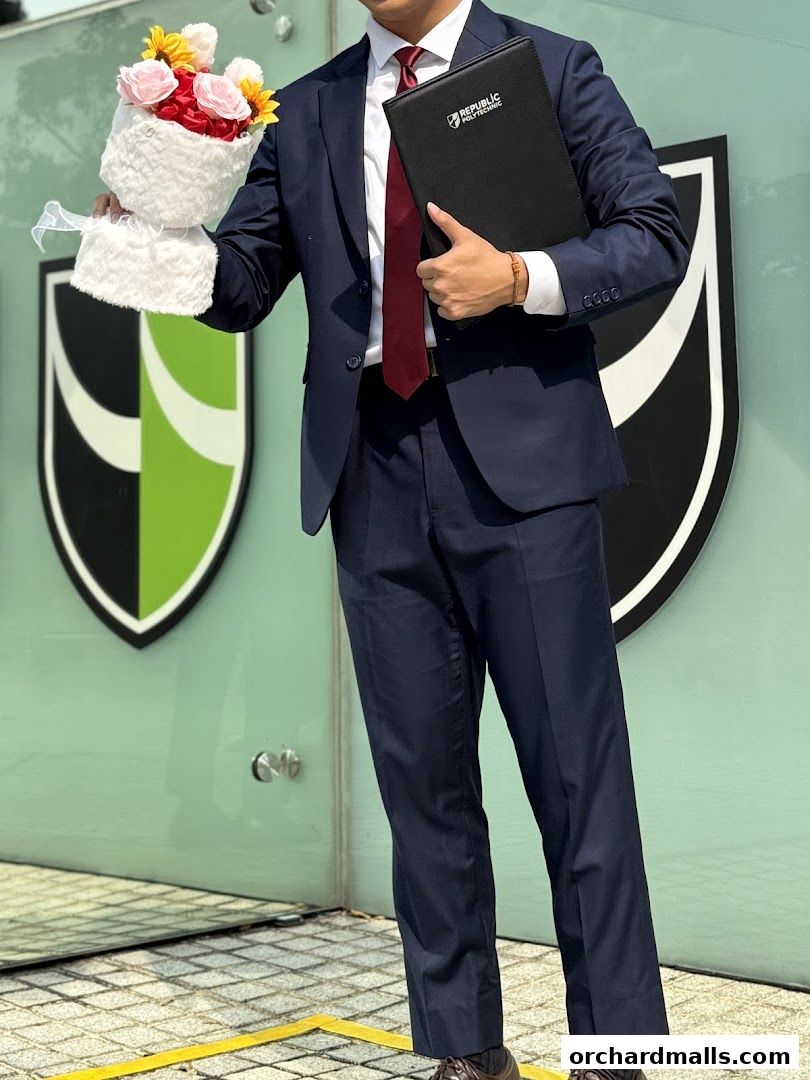 A person in a suit holds a bouquet and a folder with a logo.