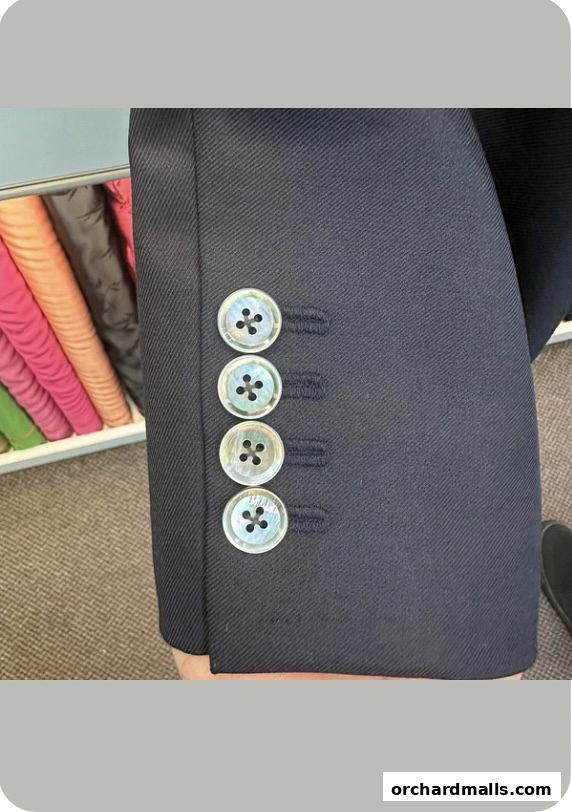 Close-up of a navy suit sleeve with four mother-of-pearl buttons and a rack of colorful fabrics.