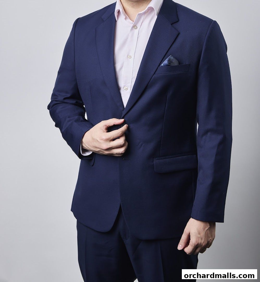 A man in a navy blue suit and pink shirt, adjusting his jacket.