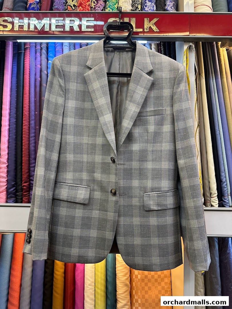 A grey plaid blazer is displayed in front of a wide selection of colorful fabrics.