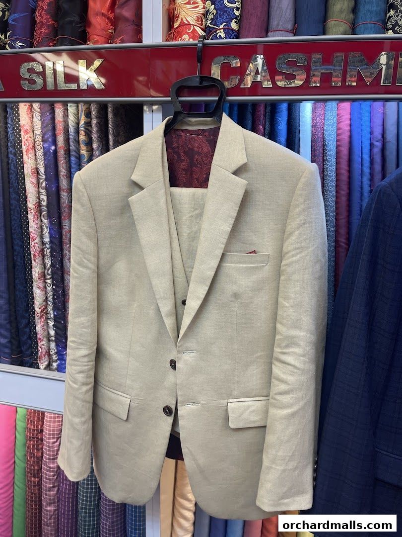 A beige linen suit is displayed in front of a wall of colorful fabrics.