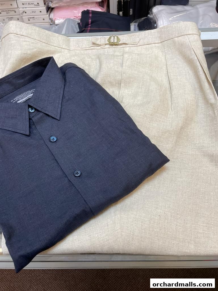 A neatly folded dark blue shirt rests on a pair of light beige tailored trousers.