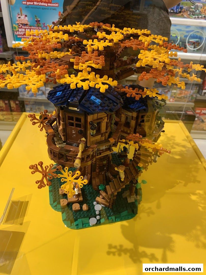 A detailed LEGO model of a treehouse with autumn foliage displayed on a yellow surface.