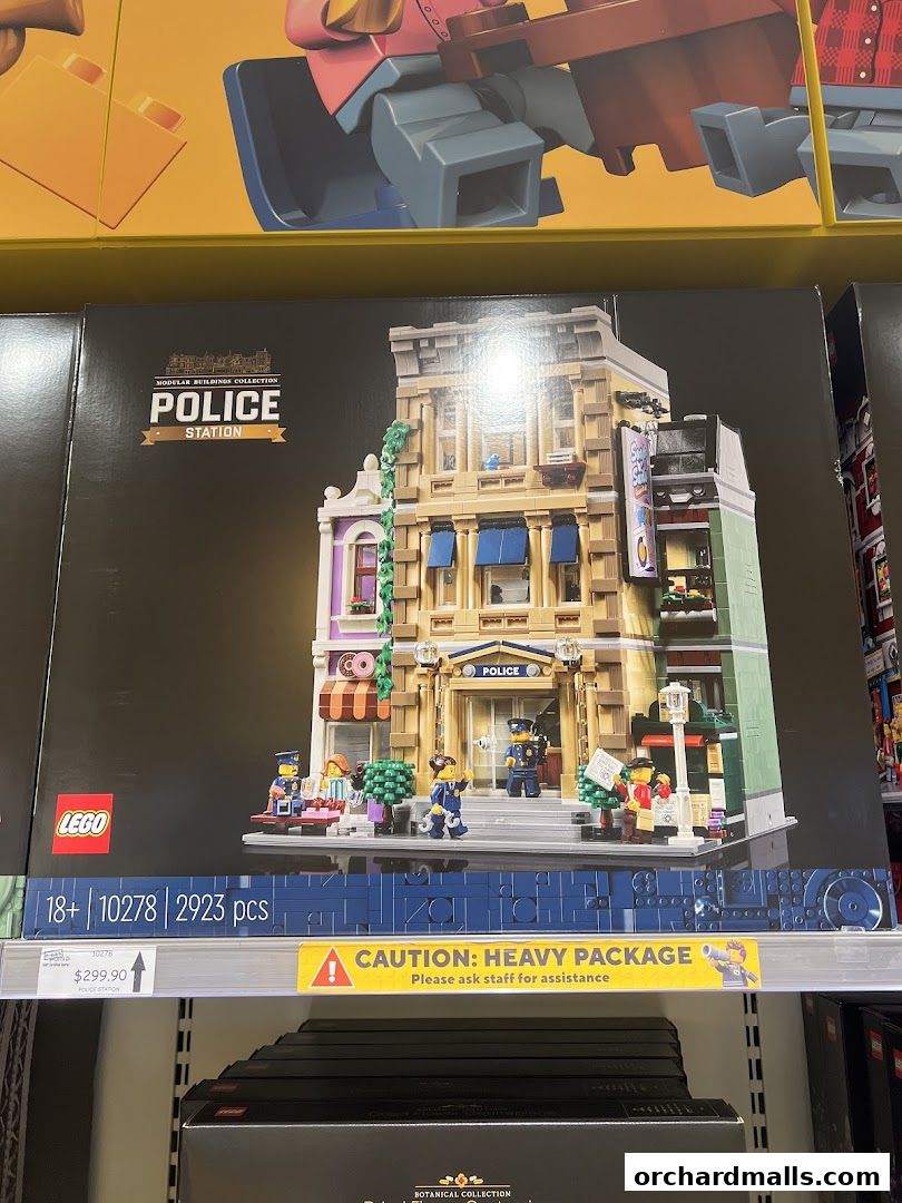 A LEGO Police Station building set is displayed on a shelf with a price tag and caution notice.