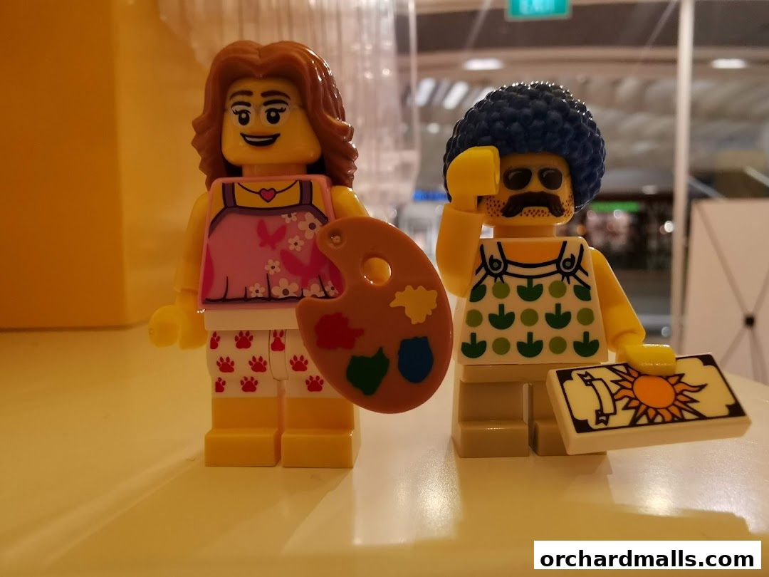 Two LEGO figures, one with a painter's palette and the other holding a sun-themed card.