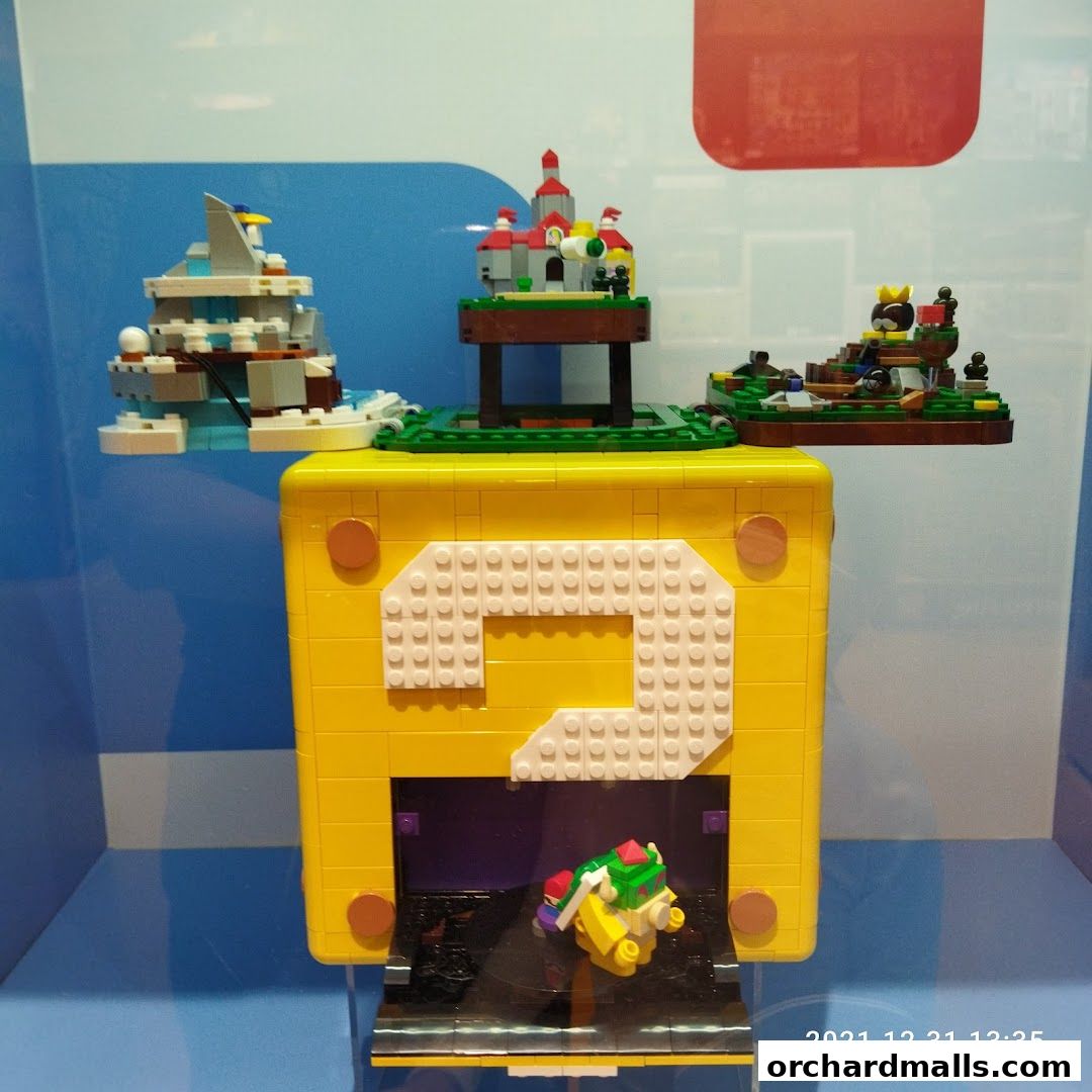 A LEGO display featuring a large yellow question block with Mario-themed dioramas.