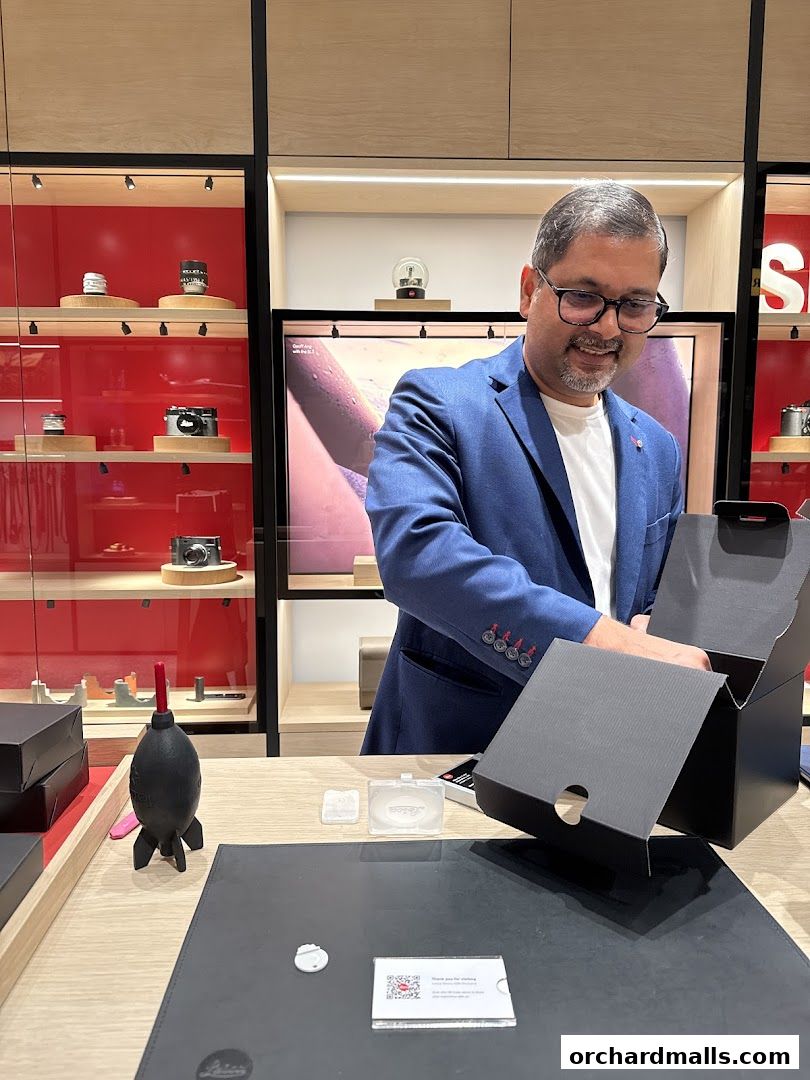 A man in a blue suit opens a box in a Leica store, with cameras displayed.